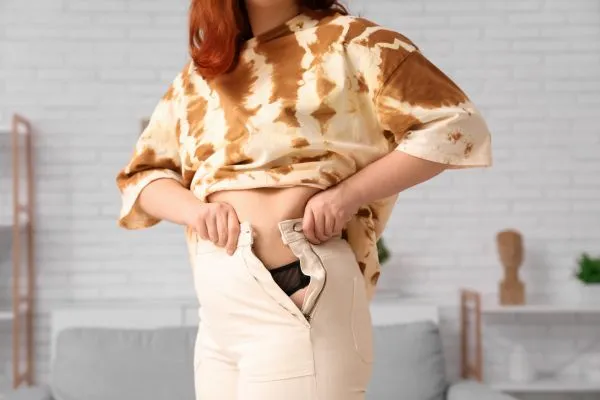 Image of woman trying to do her trousers up after pregnancy weight gain Ampthill