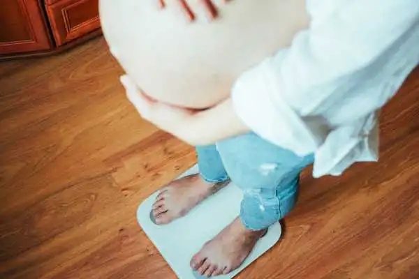 Image of woman weighing herself and experiencing weight gain through pregnancy Ampthill